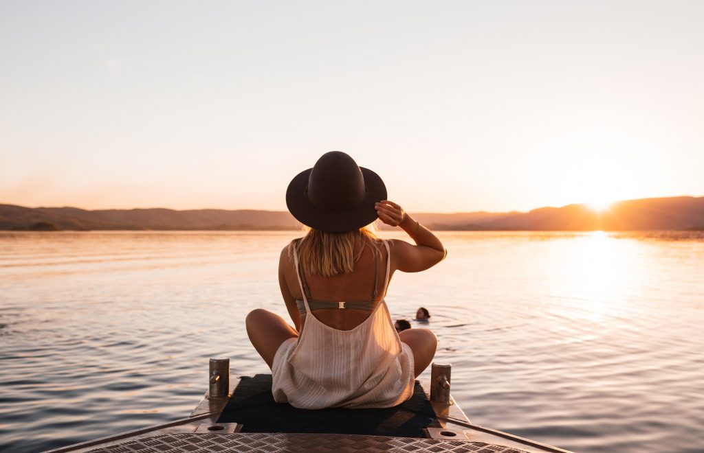 woman sitting lake pier surrounded by hills at sundown
